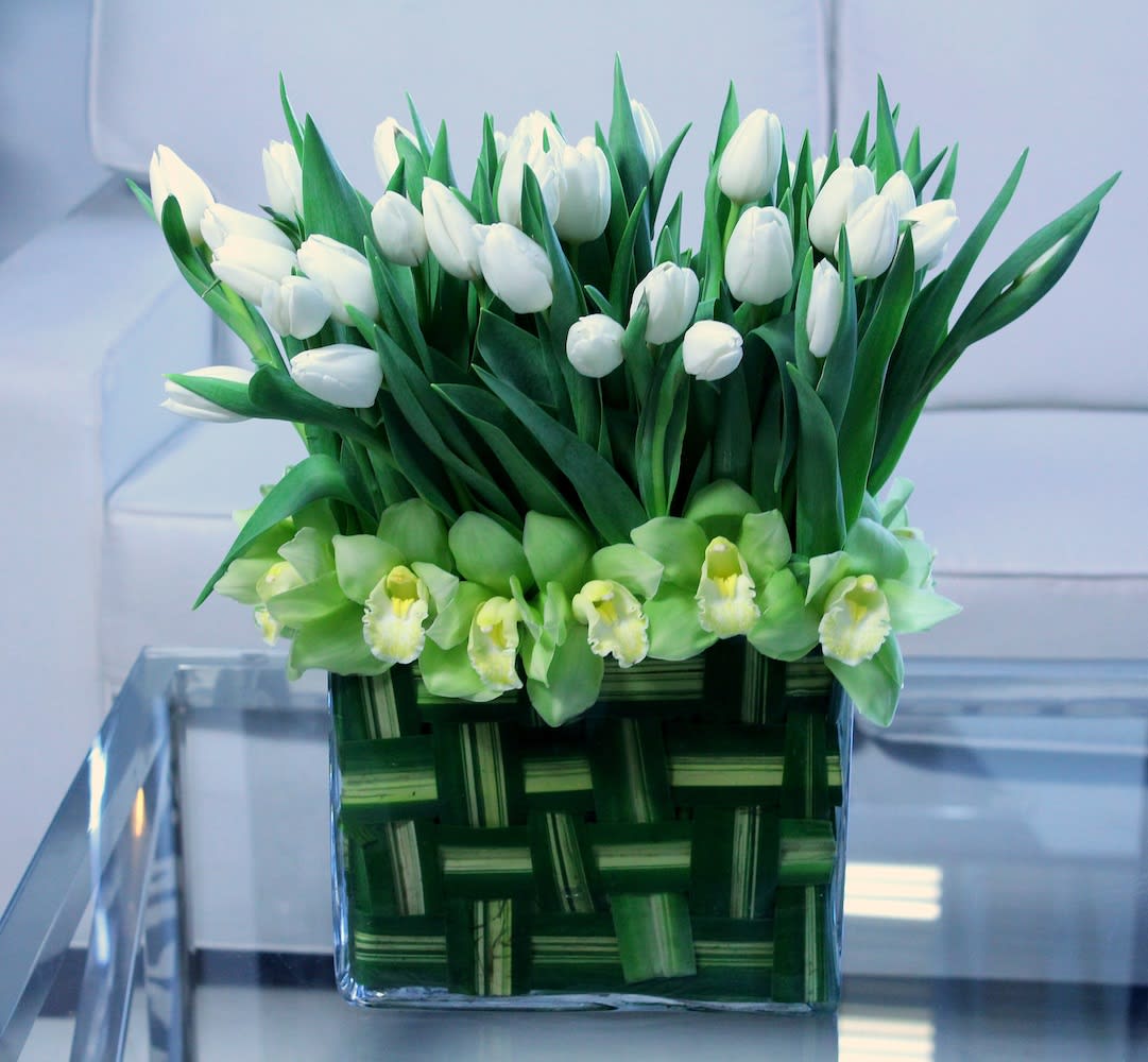 Patchwork Tulips - White tulips and green cymbidium orchids resting in a rectangular glass vase lined with a weave of verigated flax leaves.