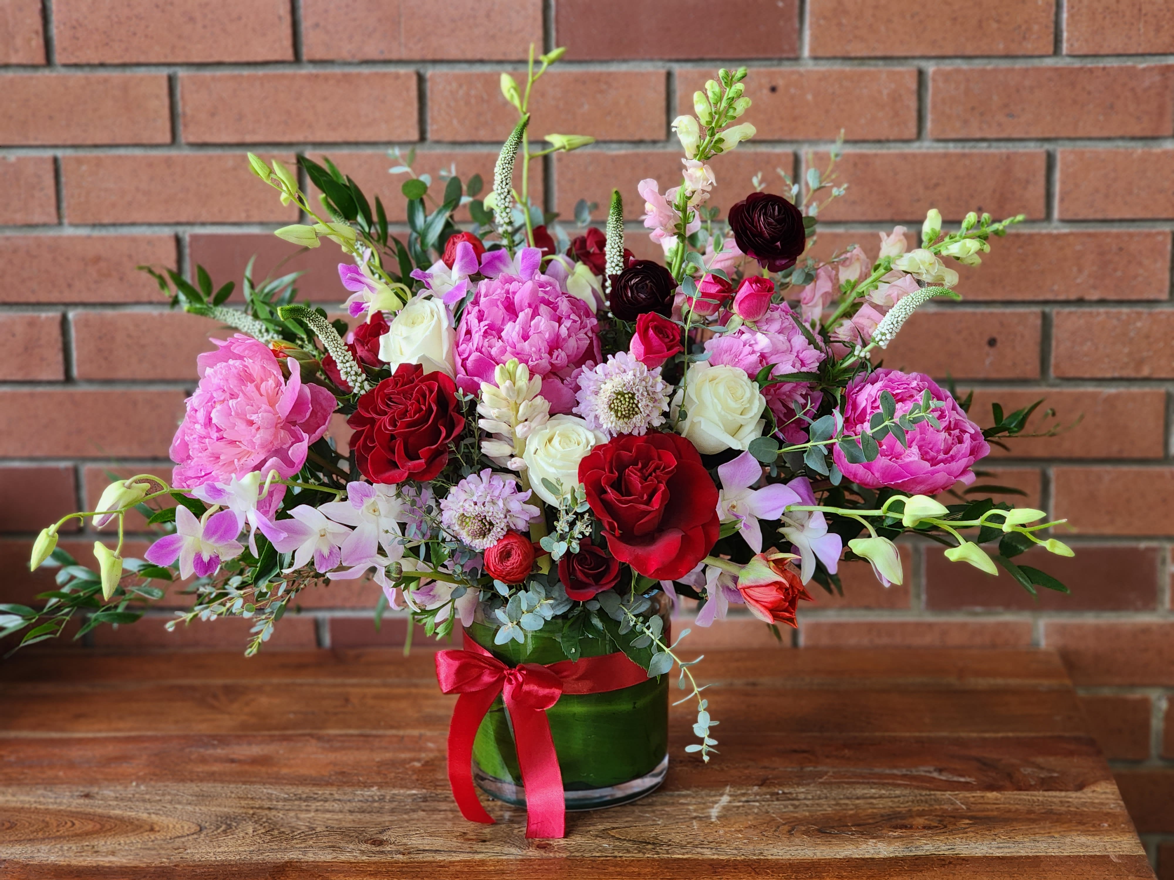 Beaming With Love Bouquet  - When you truly want to take their breath away, send this mesmerizing romantic Valentine's bouquet. Its artistic, organic design, luxurious blooms, lush selection of peonies, roses, orchids, wildflowers and more set it apart from the rest! This dramatic bouquet features red roses, dark red spray roses, burgundy ranunculus, snap dragons, scabiosa, peonies, dendrobium orchids, lush greenery and Eucalyptus. 