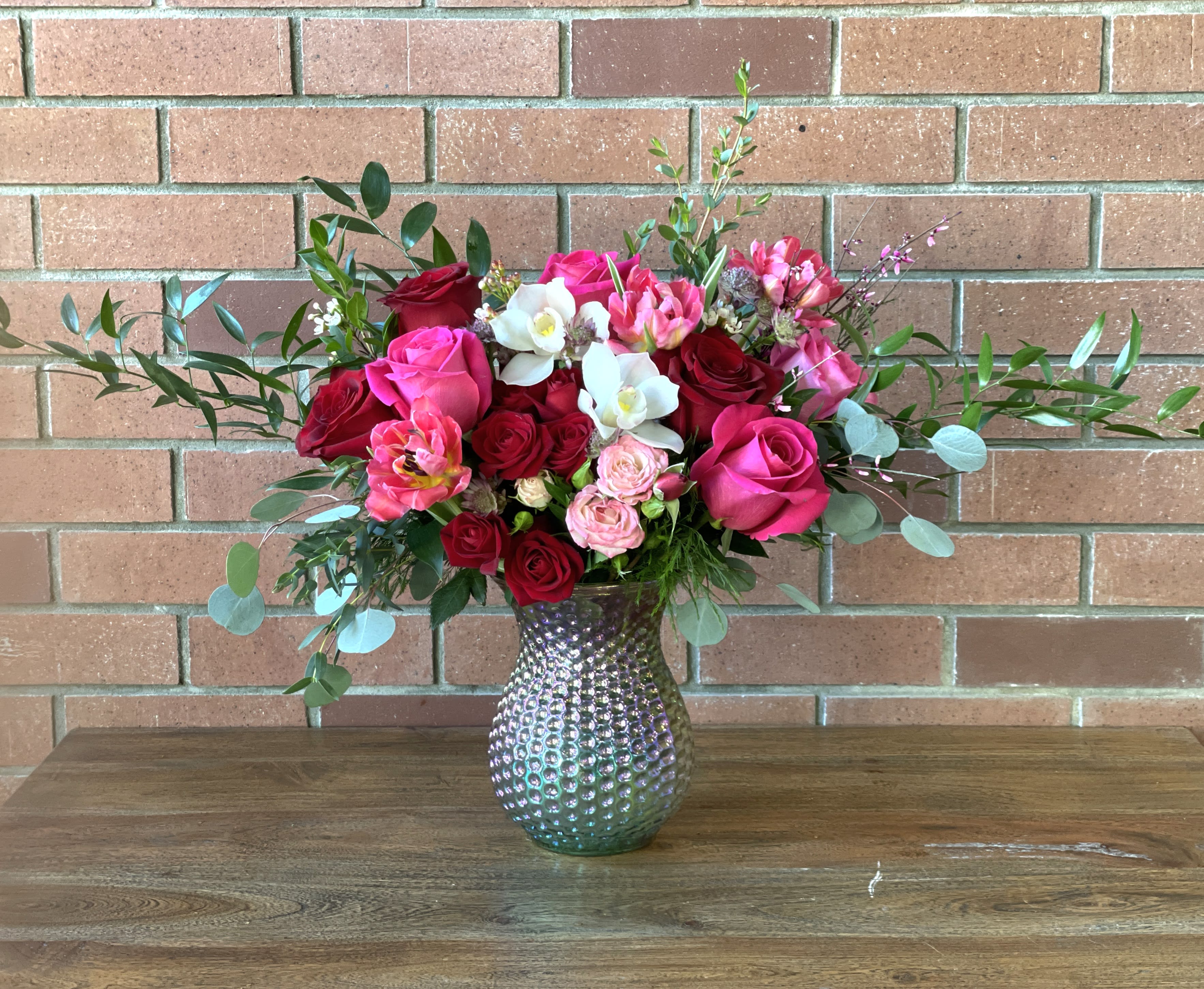 Lots Of Love Bouquet - Valentine's day bouquet arranged with red roses, spray roses, hot pink roses, tulips orchids lush greenery and filler flowers in a pretty irredecent pink vase. Standard as pictured - deluxe and premium get extra roses, spray roses, tulips and or chids worth the price increase value to make it even taller and fuller.