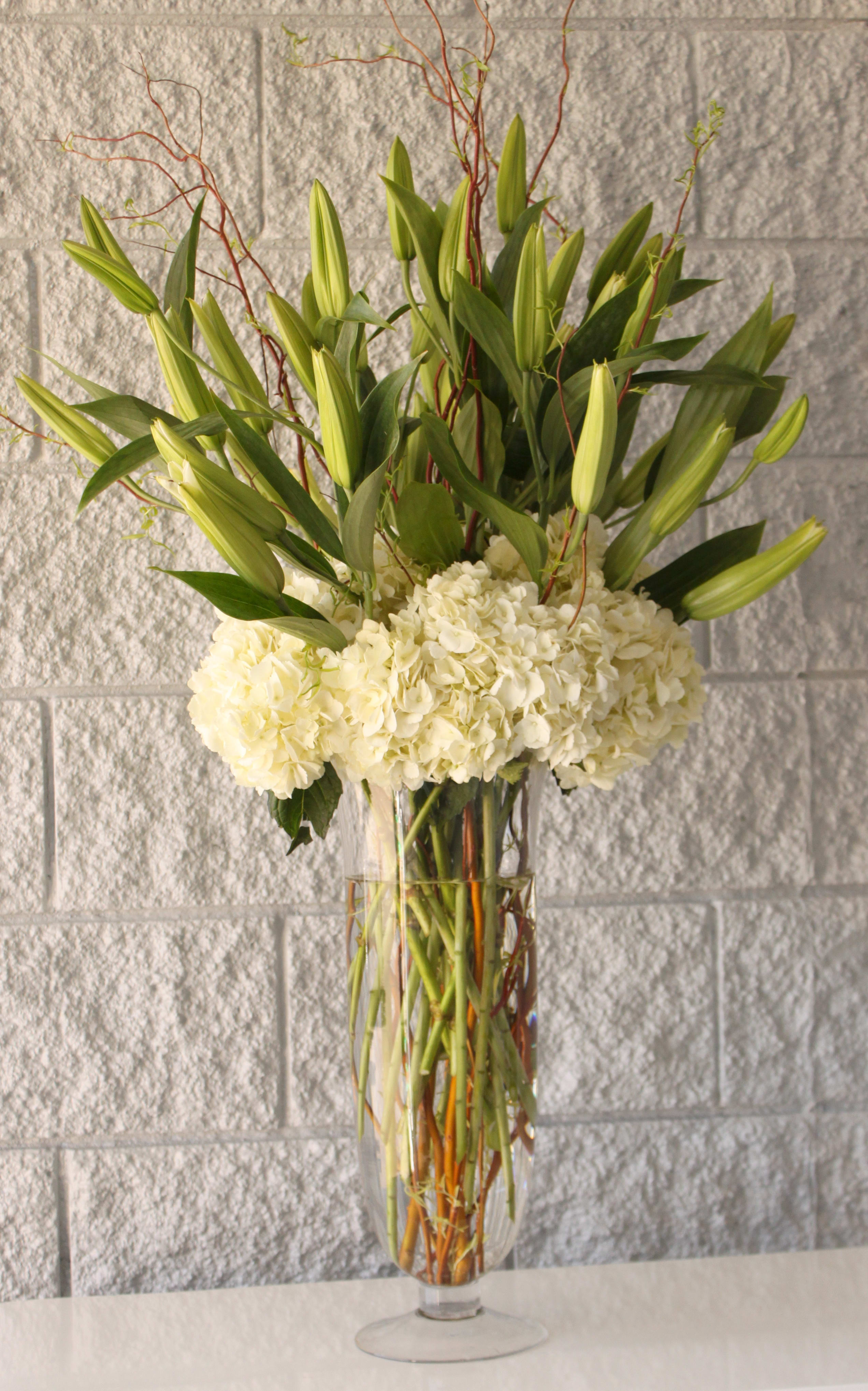 Pure Grace - A striking arrangement of tall white hybrid lilies and curly willow, accented by a base of white hydrangea. Stems of the curly willow may not always be available and subject to availability of other woody stems as a replacement.    