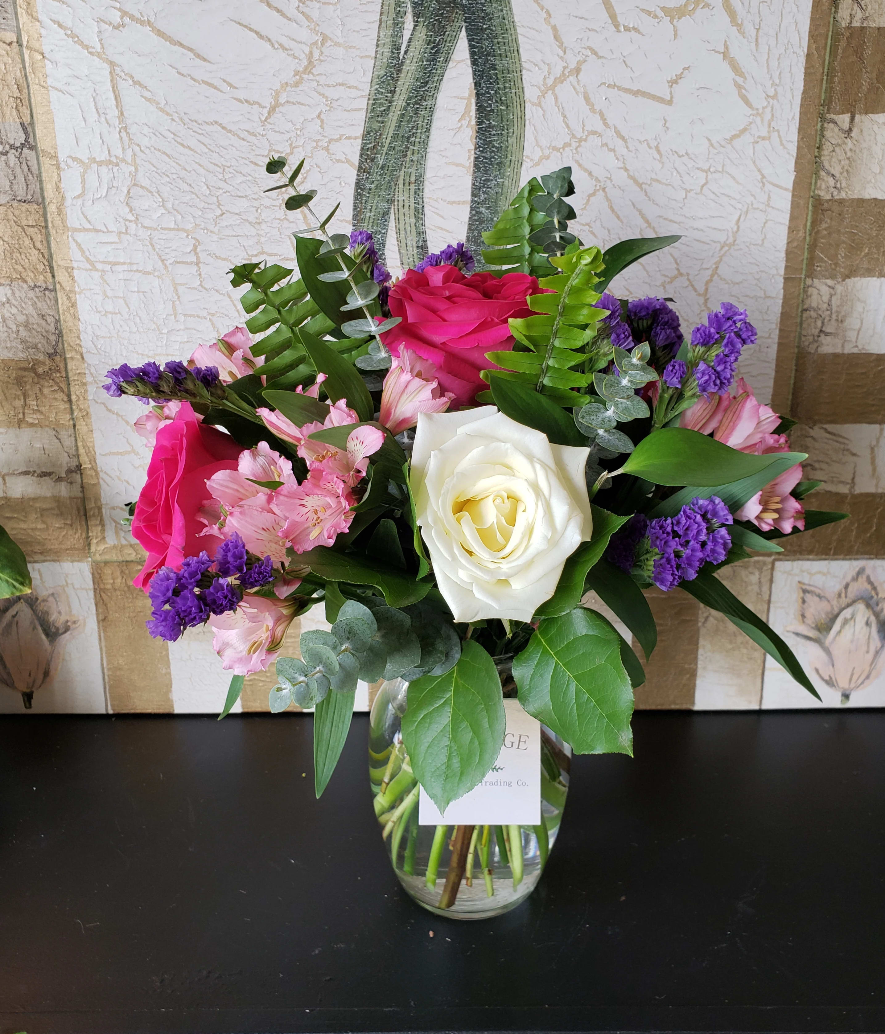 Colette - Colette is tastefully arranged in a clear glass vase. For custom orders and upgrade options, please contact our shop directly at 732-341-3723.  Lemon Leaf, Sword Fern. Israeli Ruscus, Eucalyptus, White and Hot Pink Roses, Pink Alstro and Purple Statice.