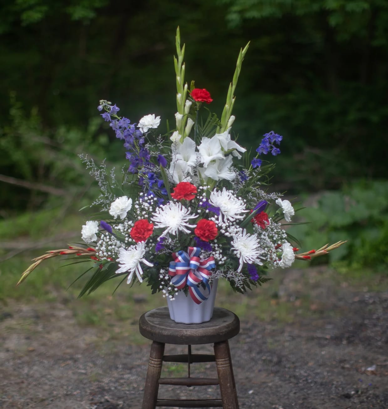 Memorial Mache Red White and Blue - A traditional fresh arrangement of red white and blue. Commonly used for the cemetery stones of veterans on Memorial Day weekend. These are also a wonderful tribute to send to calling hours for veterans or someone who was very patriotic. Flower varieties may vary from photo.   