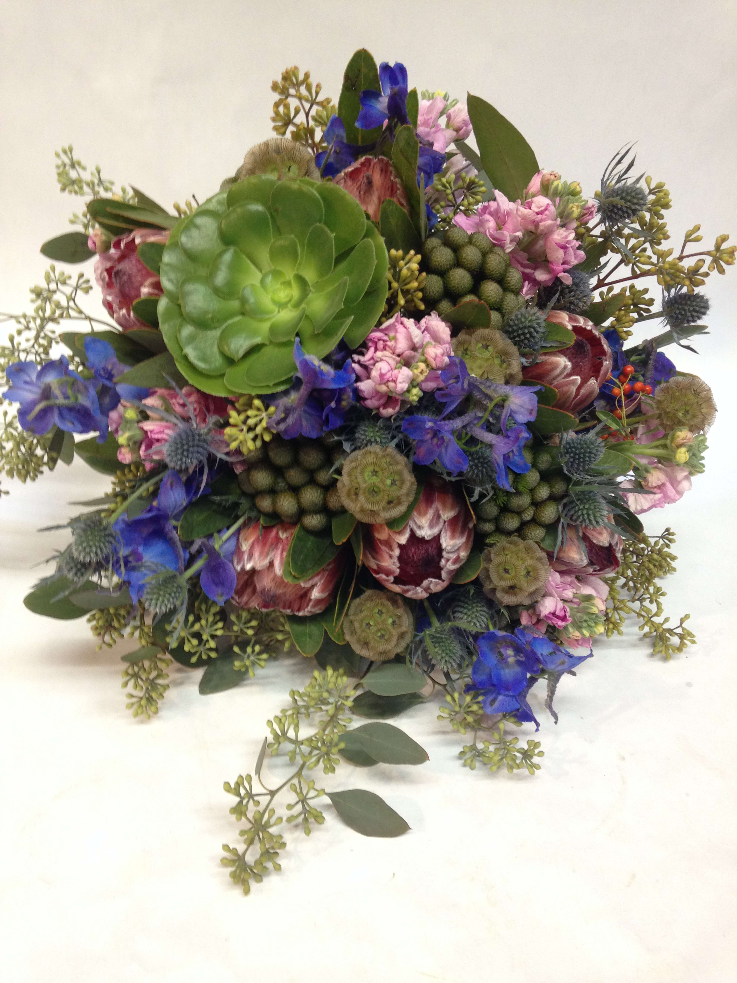Something Funky, Something Blue Something Funky, Something Blue - This funky bouquet mixes textures and colors in a surprising way for a creative and unique look! Featuring delphinium, thistle, succulents, protea, scabiosa, and other seasonal greens. Featured Bouquet: $345.00