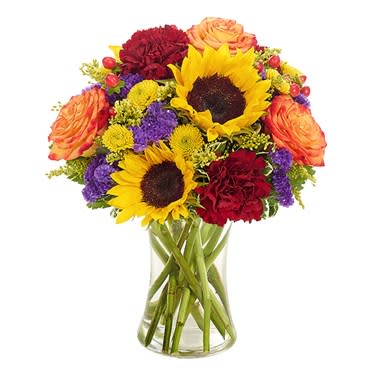 Fiery Fall Bouquet - Fall is a season unlike any other, bursting forth with a kaleidoscope of glowing color. This innovative bouquet captures the colorful expressions of fall...showcasing sunflowers, roses, button poms, carnations, yarrow, statice and hypericum in a lovely gathering vase. Measures 12”H X 13”L. Suggested Retail Price: $59.99.