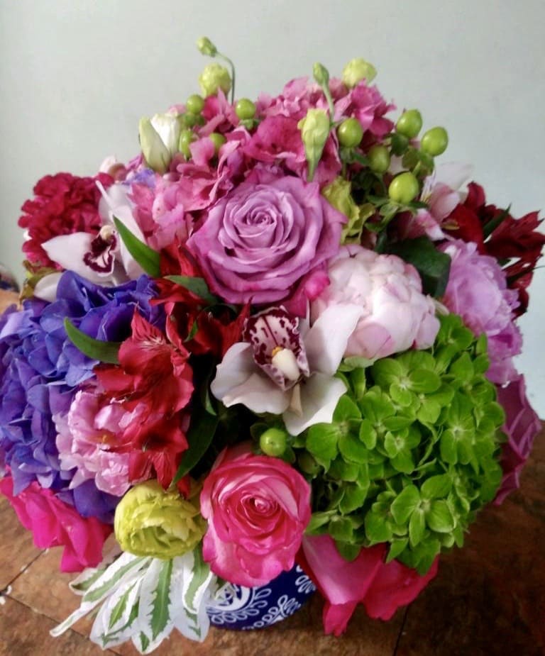 Ready to Bloom Ready to Bloom - This arrangement contains pink peonies, green and purple hydrangeas, purple roses, green coffee beans, and cymbidium orchids all arranged in a ceramic vase.