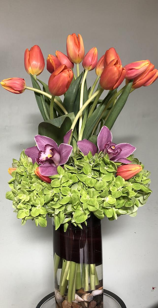 Brilliantly Orange Brilliantly Orange - Orange tulips, green hydrangeas, purple cymbidium, all hand arranged in tall glass vase.