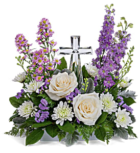 Poised with Love Bouquet - Soft and serene, this artistic array of cream and lavender blooms around a radiant crystal cross keepsake is a heartfelt expression of love. This beautiful piece includes crème roses, lavender larkspur, lavender montecasino asters, white cushion spray chrysanthemums, lavender sinuata statice, lemon leaf and dusty miller. Delivered with Teleflora's Small Crystal Cross. Approximately 16&quot; W x 16&quot; H