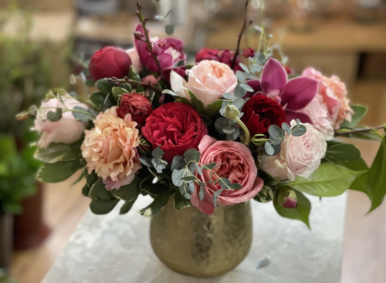 Queen of the Garden - An absolutely stunning fresh flower arrangement full of premium and garden roses, orchids and delicate greenery. Artfully arranged in a quality hammered metal gold toned vase. This will stand out from the crowd. 