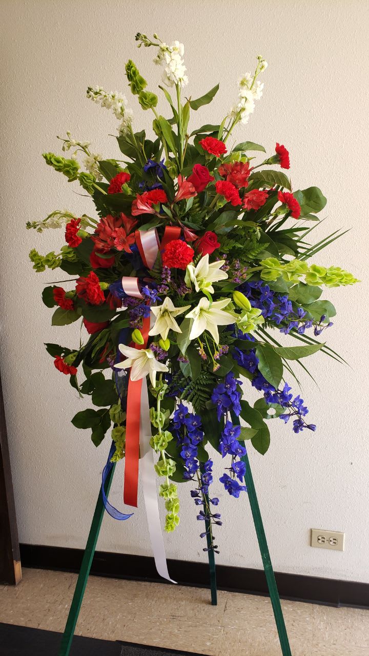 the tribute the tribute - 5 white stock, 6 stems bell of ireland , 5 stem dark blue delphinium ,2 white Asiatic lilies ,10 red carnation,5 red roses,4 red astromelia 2stem of purple statice. 1 wire easel with a tricolor bows blue, white and red