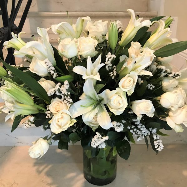 Grand Arrangement with white roses and Lillies and other flowers - All white large arrangement with premium white roses and multi blooms white Lilies with other flowers elegantly arranged with greenery in a tall glass vase.   The quantity of flowers increase with Deluxe upgrade.  Much more flowers for Premium upgrade.  