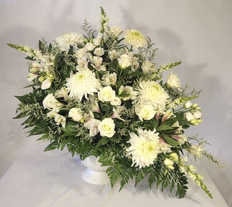 White Sympathy Basket White Sympathy Basket - This white sympathy basket is a beautiful statement of peace and comfort. White roses, lisianthus, snapdragons, mums, limonium, alstromeria and lilies are accented with a assortment of greenery in a white plastic urn. A beautiful way to honor the life of the deceased.