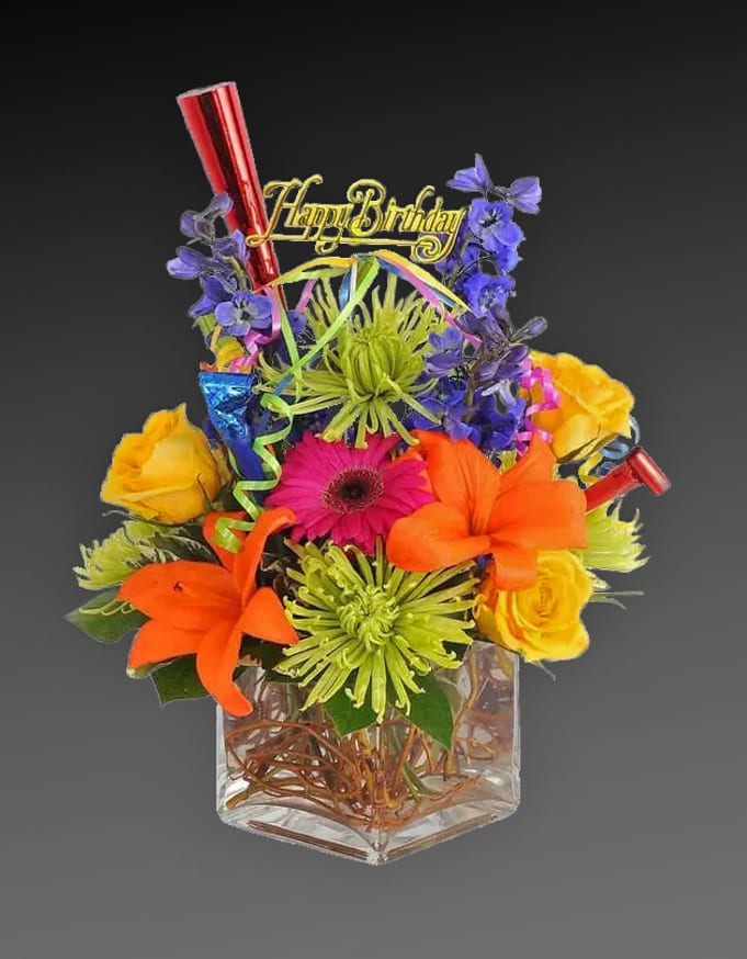 Birthday Smile - A bright and cheerful bouquet of seasonal blooms with a Happy Birthday pick, streamers and a noisemaker or two! 5&quot; glass cube vase.