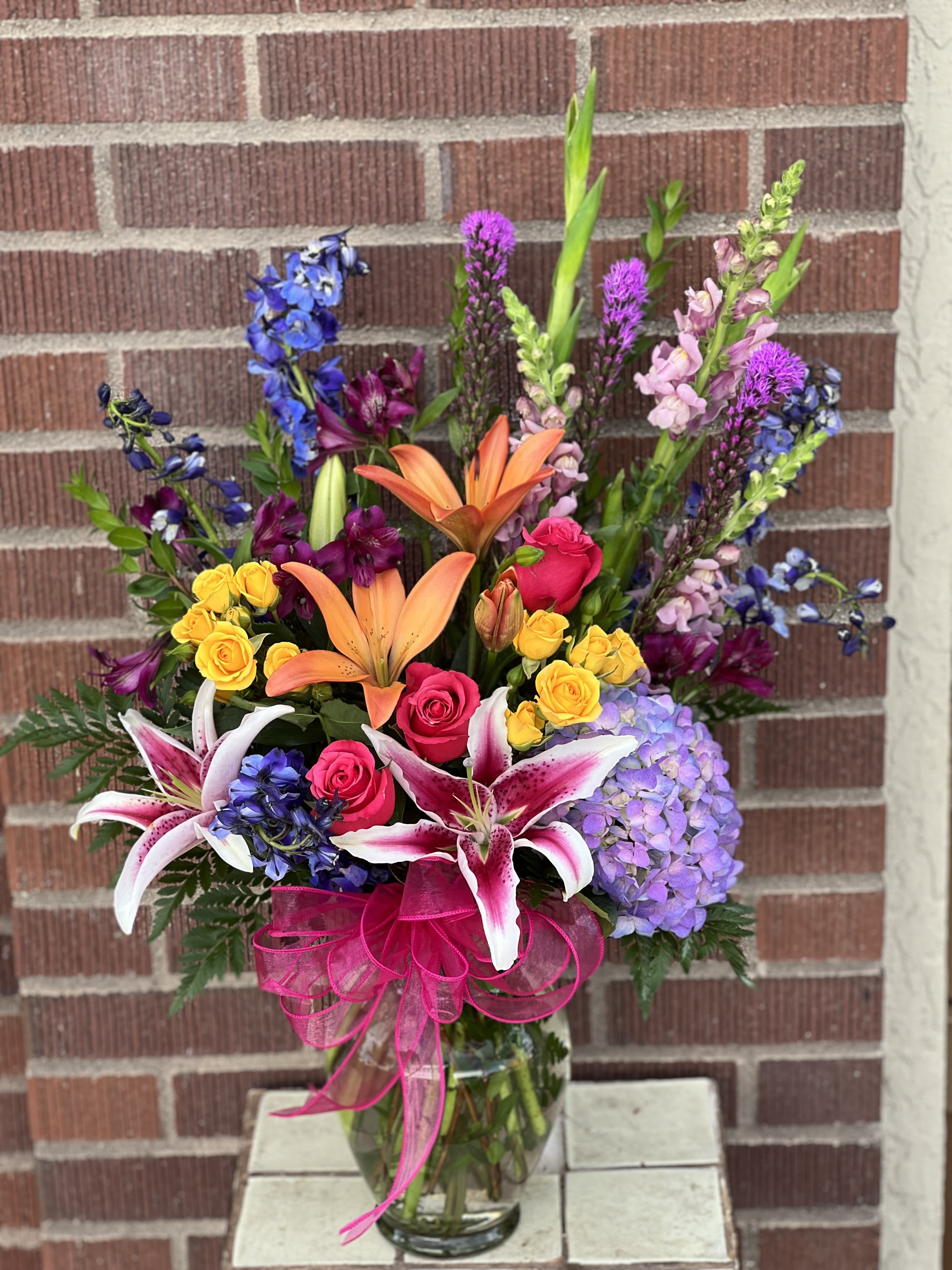 Colors Of The Rainbow Colors Of The Rainbow - This colorful bouquet includes purple hydrangea, pink roses, yellow spray roses, orange asiatic lilies, purple alstroemeria, blue delphinium, pink snapdragons, blue eryngium, huckleberry, oregonia, Israeli ruscus, sword fern, silver dollar eucalyptus, seeded eucalyptus, and lemon leaf. Delivered in a jordan vase. Approximately 22" W x 28 1/2" H Product ID: T282-9A