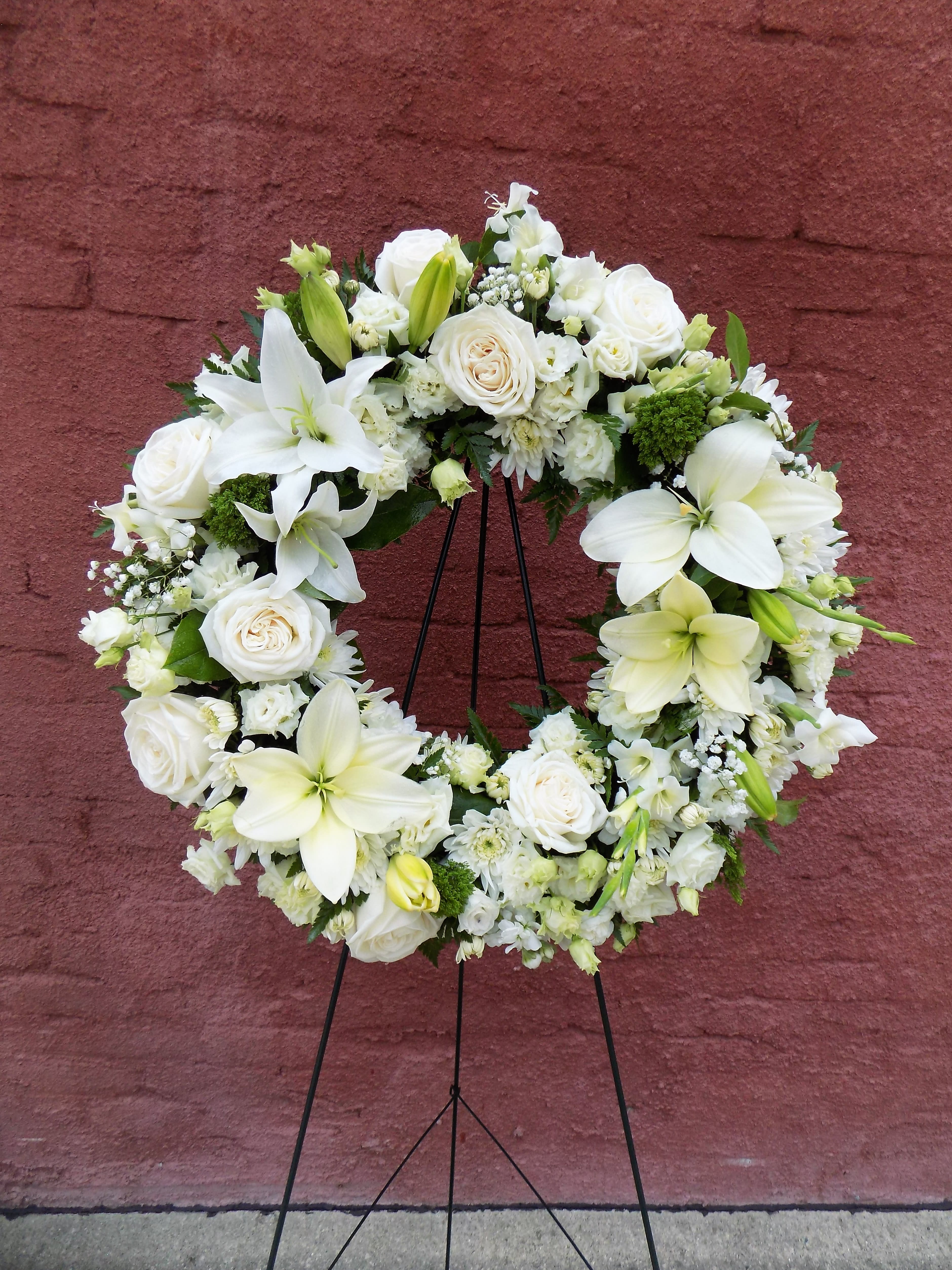 Circle of Serenity - An all-white standing spray wreath featuring a peaceful array of white blossoms. Roses, lilies, mums, and babysbreath come together into a serene and beautiful design! We specialize in custom-designs, and this arrangement can be designed in an array of different colors. Please call us at 320-587-3110 to customize this design, and we will do our best to accommodate all requests! 