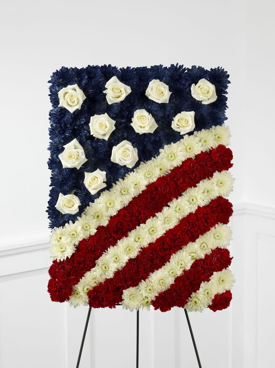 TLSP The Glory Be Flag Tribute - The Glory Be Flag Tribute is a symbol of patriotic beauty to commemorate the life of your loved one at their farewell service. Red carnations, white chrysanthemums and blue dyed white chrysanthemums create a stirring arrangement in the likeness of the American flag with white rose accents to symbolize the stars. Displayed on a wire easel, this exquisite arrangement will bring comfort and peace to their family and friends. Approximately 24&quot;H x 18&quot;W.  Your purchase includes a complimentary personalized gift message.