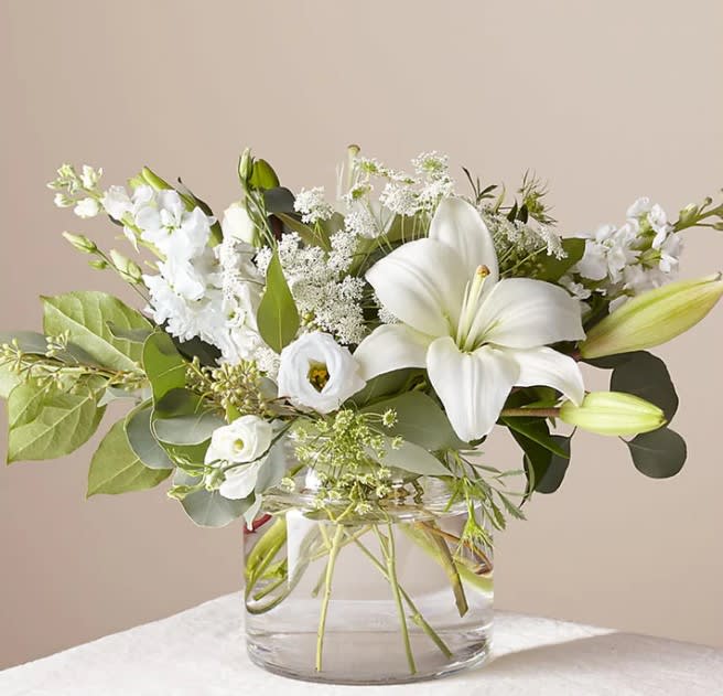 Angela - An illuminating array of florals brings an air of elegance to any room it's placed. This arrangement features refined florals like lilies, Queen Anne's Lace and Veronica in a clear glass vase to add a touch of sophisticated style to your special occasions.  BLOOM DETAILS Eucalyptus, Lily, Queen Anne's Lace, Stock, Veronica