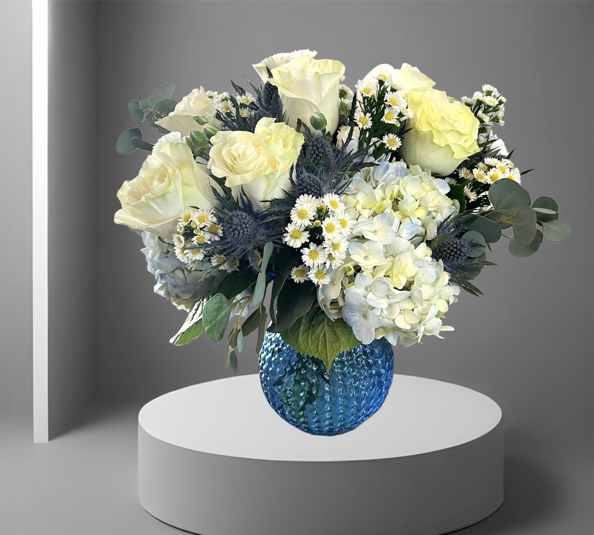 Baby Blue - A beautiful mix of baby blue hydrangea, white roses, blue thistle, and accent foliage arranged in a blue vase.  A perfect way to welcome a new baby, say thank you, or express sympathy.