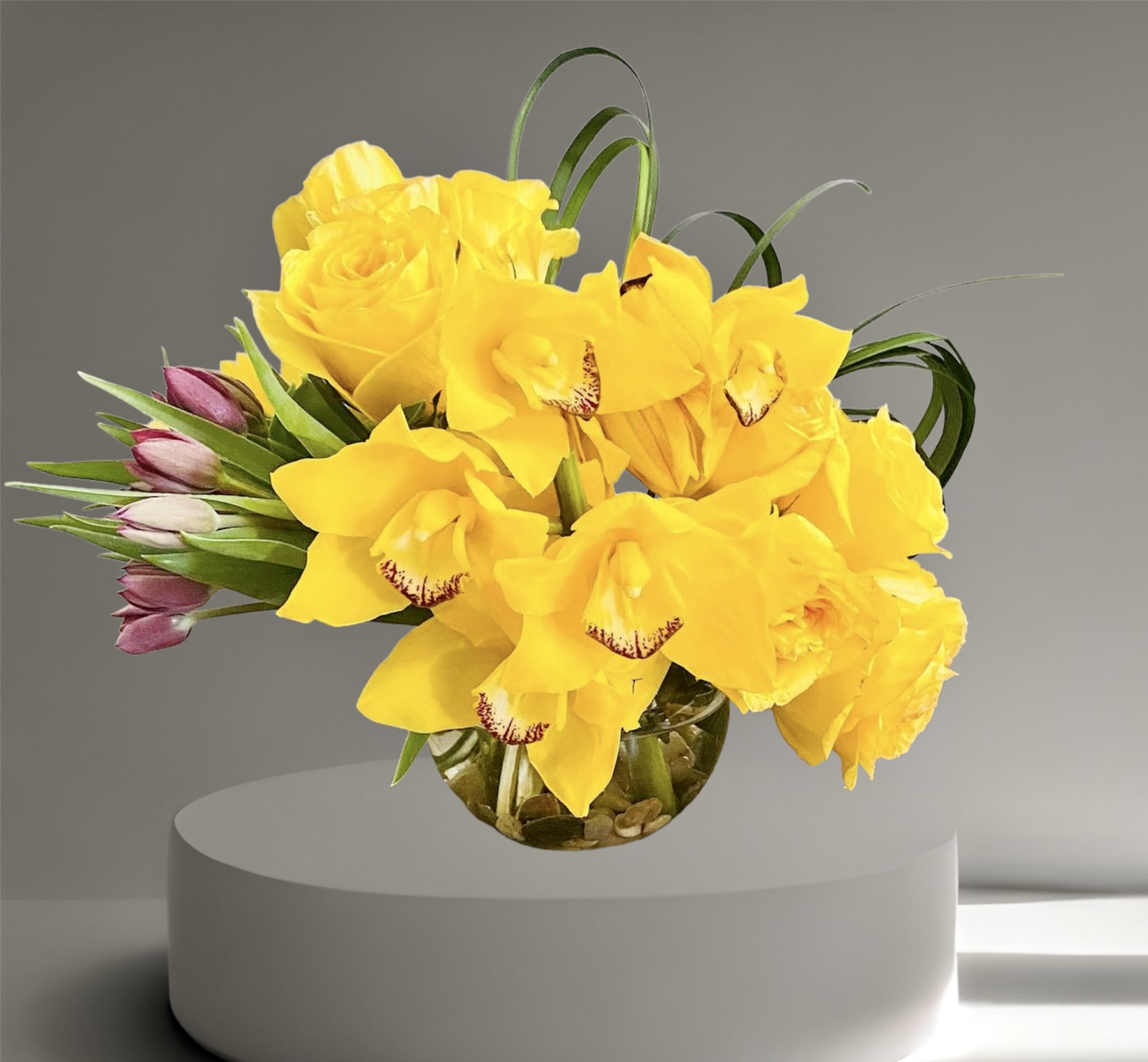 Sunburst - A bright, happy arrangement of roses, tulips, and orchids. Arranged in a glass bowl accented with river rocks and lily grass. The perfect pick-me-up or cheery gift!