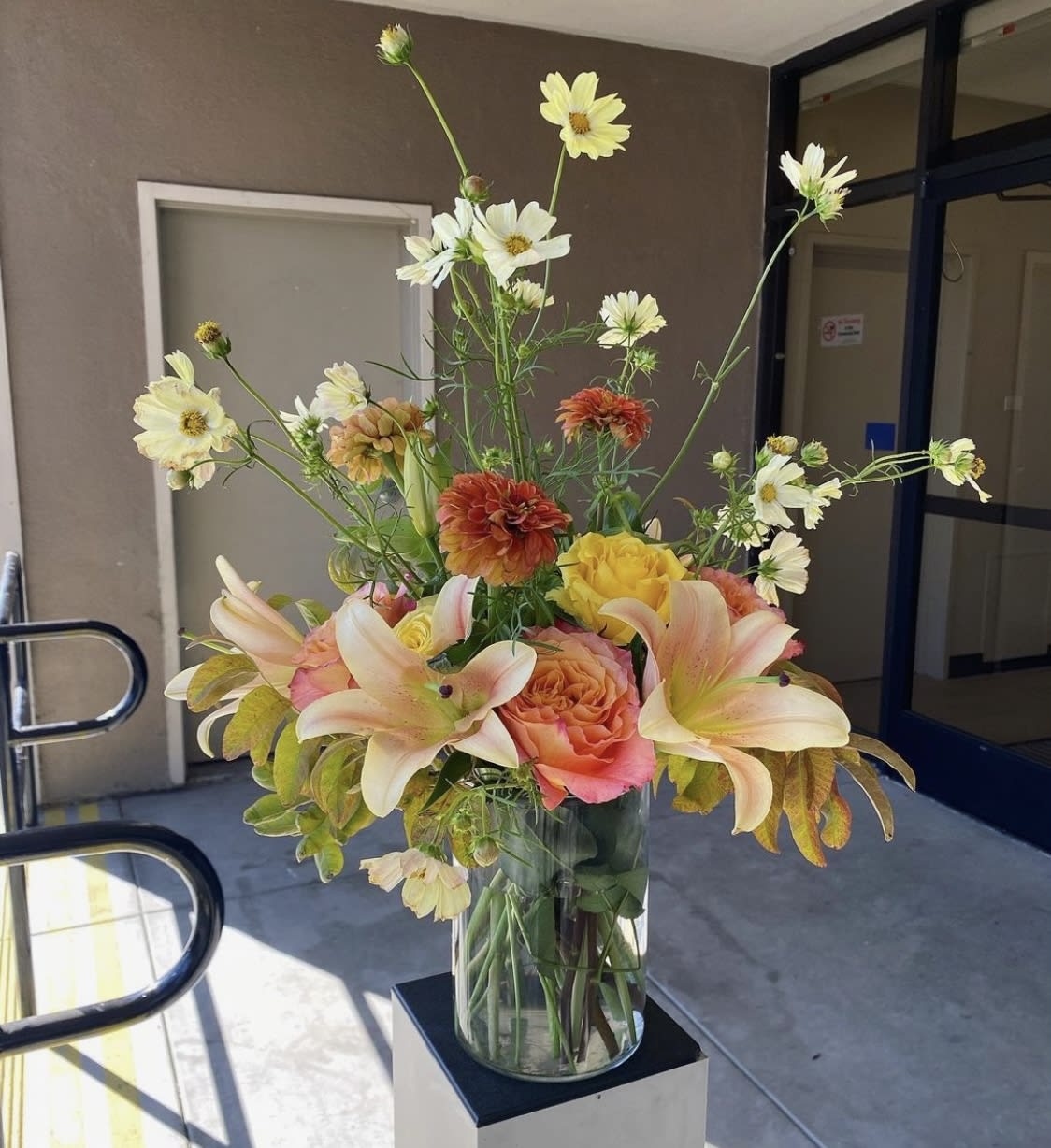 Fall into Summer - Celebrate Summer with this arrangement featuring zinnias, lilies, cosmos, and pistachio leaves. Comes in a clear glass vase.