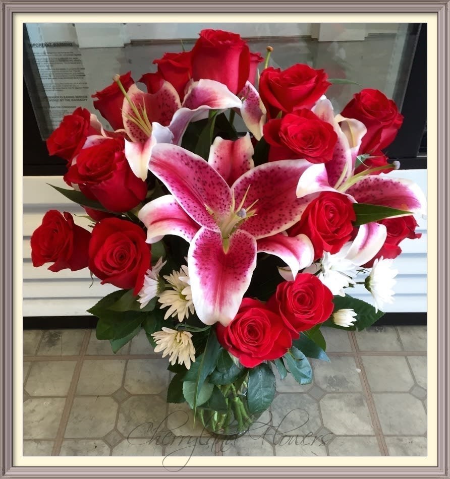 CF832 - Cupid's Masterpiece features a fresh combination of red roses, pink stargazer lilies, white daisies, and foliage artfully arranged in an elegant glass vase. 