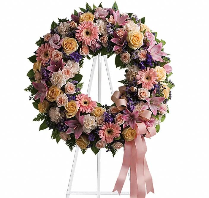Graceful Wreath - Family and friends will recollect how special their loved one was with this gentle and timeless circle of fragrant blooms to celebrate sweet memories. A mix of flowers such as peach roses gerberas and carnations pink asiatic lilies and lisianthus purple limonium and lavender larkspur nest in greens on an easel-mounted wreath.