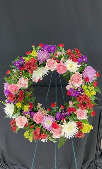 Vibrant Life Standing Wreath (Customizable) - A circular wreath covered in mixed flowers of your color choice on a bed of mixed greens. The wreath is mounted on a 4ft standing easel for prominent display at funeral services.