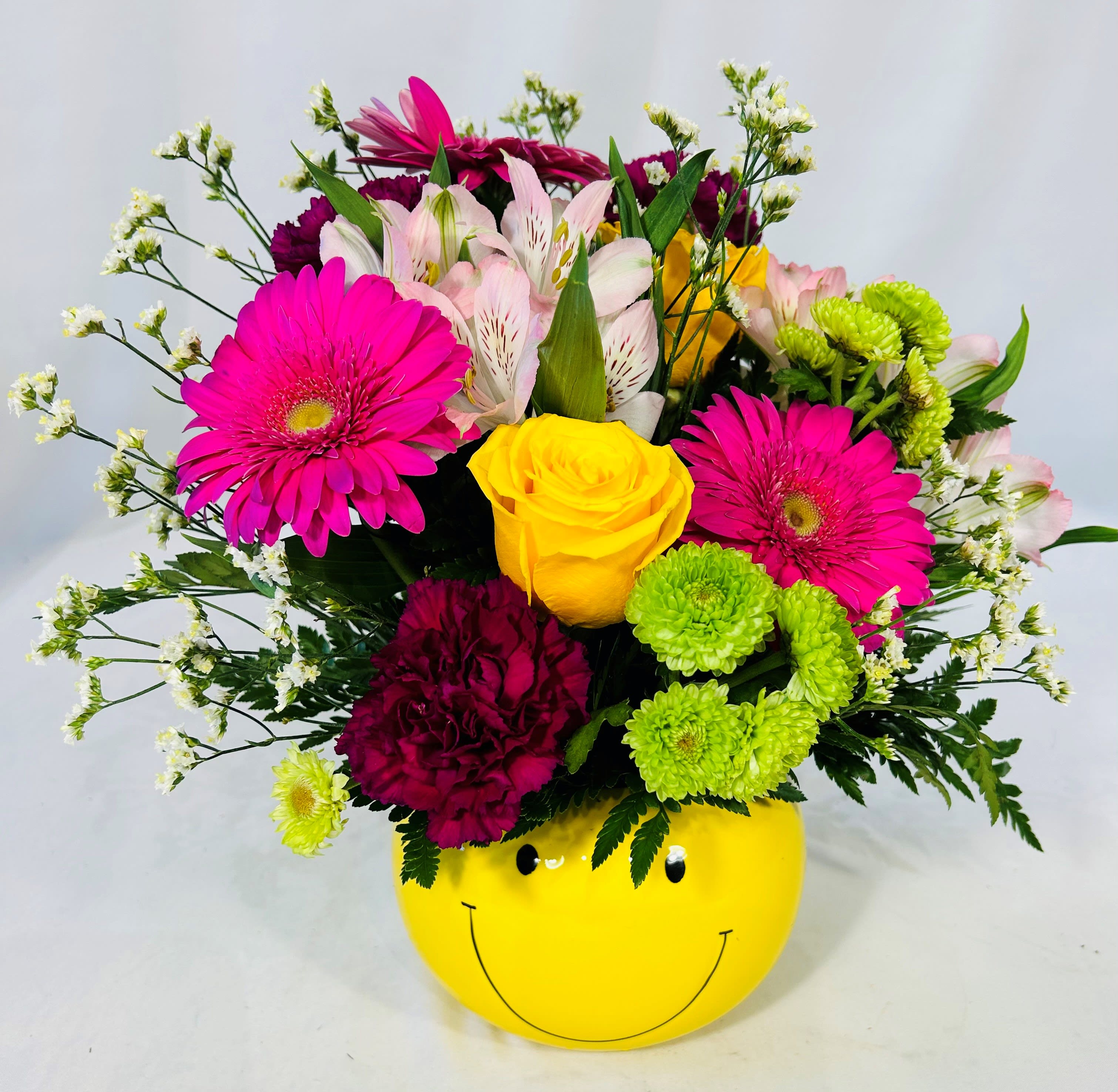 Smiley Face Arrangement - Send a smiley face arrangement to bright up someone's day. This smiley face container is ceramic and full of bright flowers like carnations, gerbera daisies, roses and filler flowers.