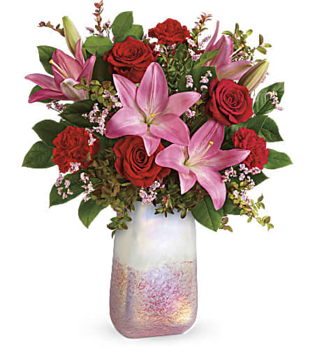 Teleflora's Pretty In Quartz Bouquet - The shimmering, iridescent art glass of this stunning rose quartz inspired, hand-blown vase is the perfect partner for a fresh, fabulous bouquet of red roses and pink lilies! This bouquet features red roses, pink asiatic lilies, red carnations, pink limonium, red huckleberry, and lemon leaf. Delivered in a Pretty In Quartz vase. Approximately 16 1/2&quot; W x 21&quot; H 