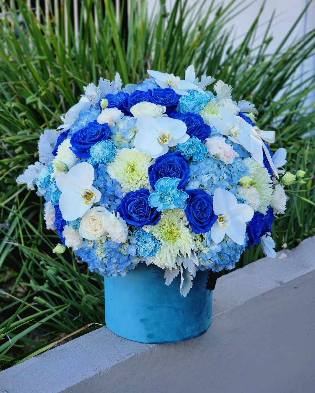 New Life  - This blue-themed floral arrangement with blue hydrangeas, roses, and carnations, complemented by white orchids, will make a wonderful and heartfelt gift to welcome a new baby into the world