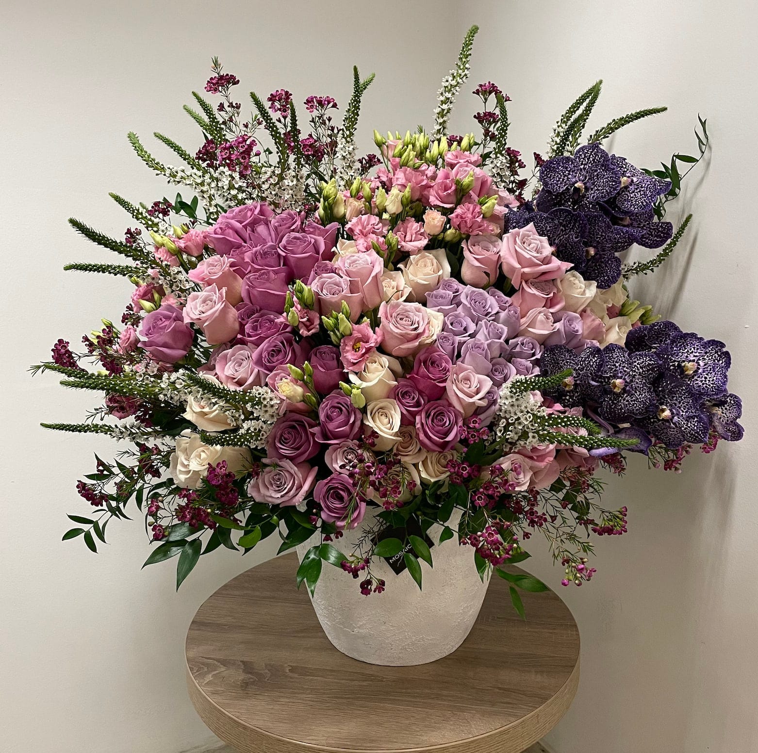 Bliss - A grand flower arrangement that brings joy for eyes and with scent. Contains an elegant mix of  roses, orchids, and other seasonal flowers and greens to create a vibrant mixture of bliss. Approximately 3 feet tall and 3 feet wide.