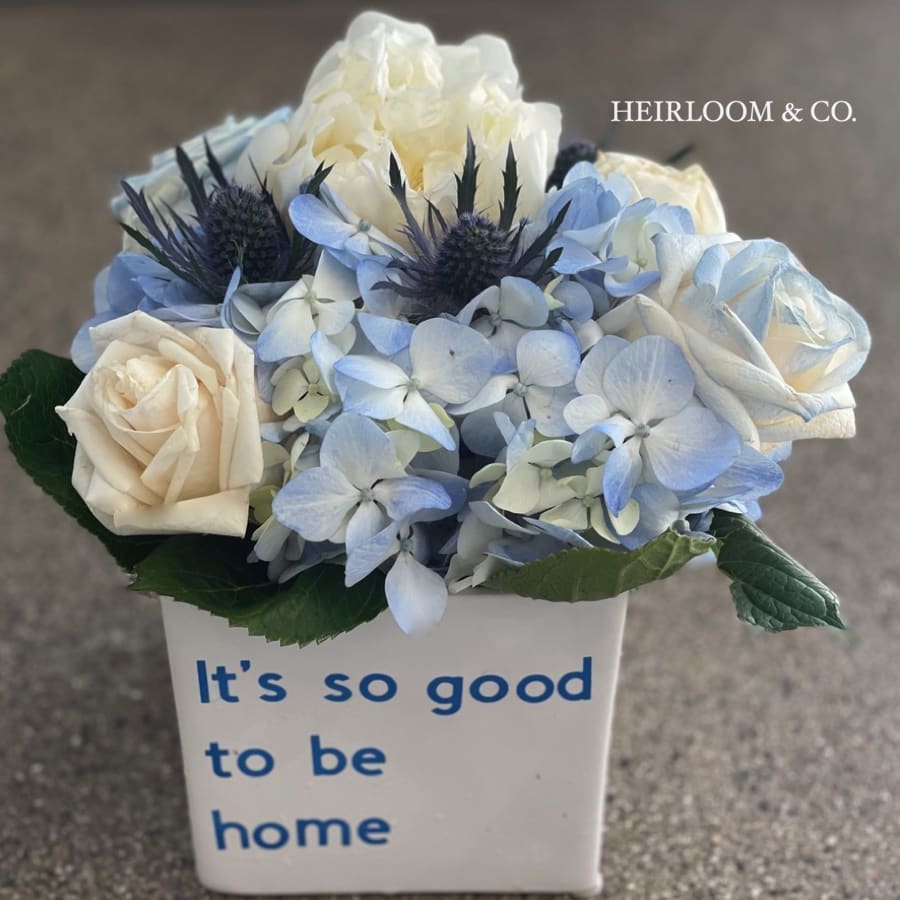 Home Sweet Home - Nothing Says Welcome Home quite like this one! Presented in white &quot;it's good to be home&quot; ceramic cube filled with exquisite handpicked garden roses in the finest of blooms, mixed beautiful blue hydrangeas, and accented with hints of thistle. Perfect for a housewarming gift,  a loved one's return home, or simply to welcome someone to your team. 