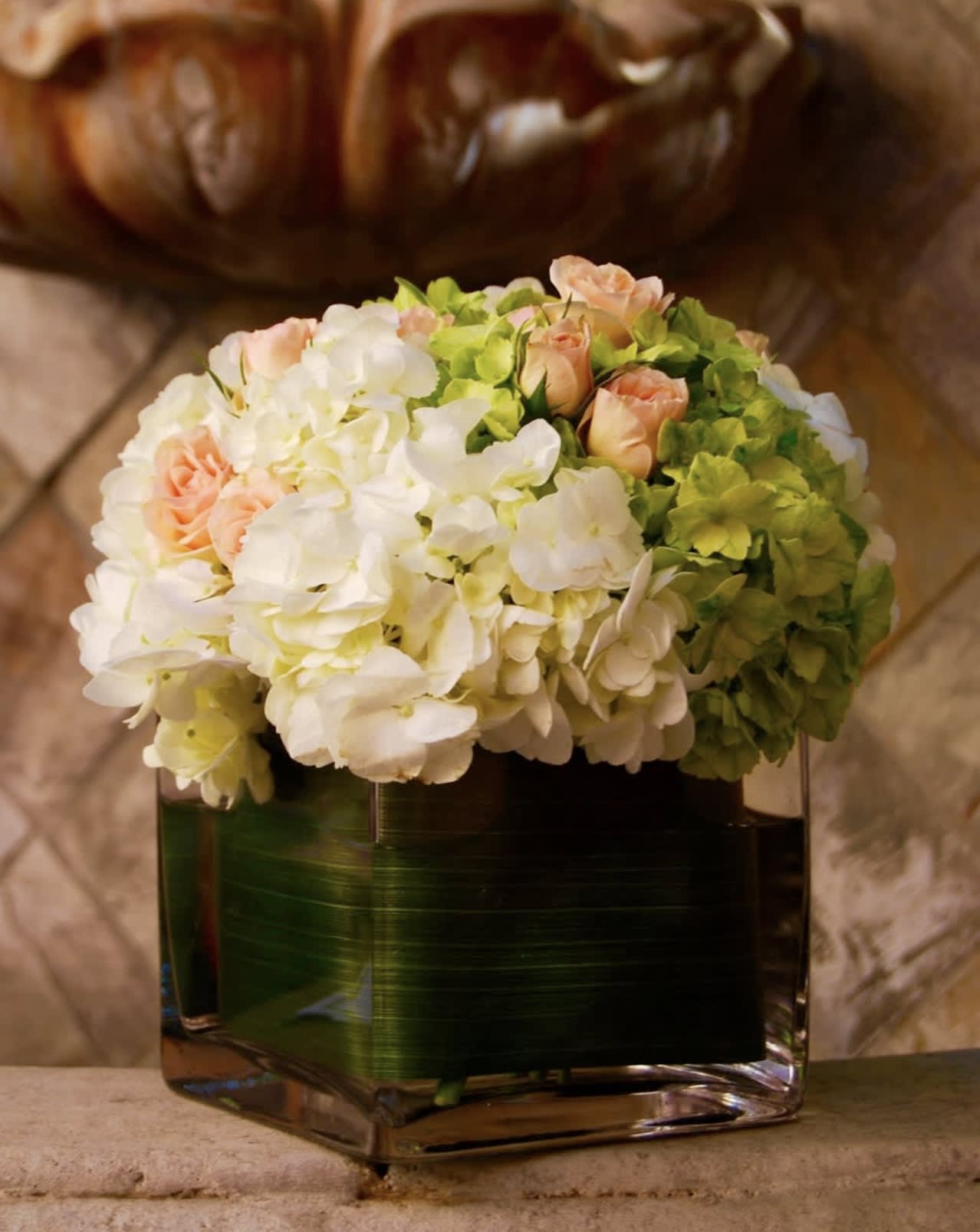 Zookies - Green and White Hydrangeas, with a sprinkle of peach spray roses, wrapped up in a cube vase with leaf ribbon lining. 