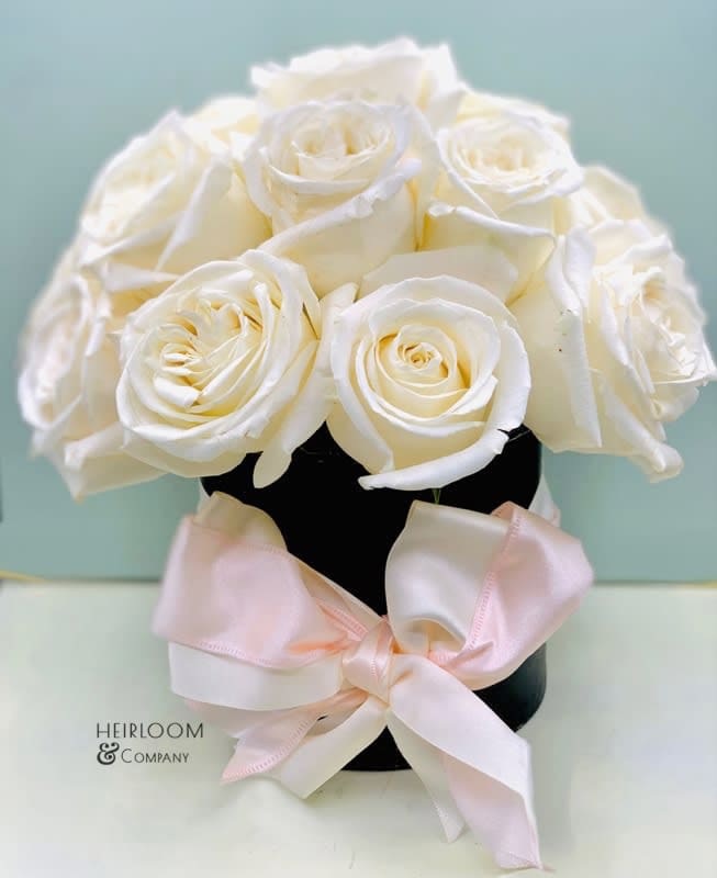 Cinderella 99 - Dreamy and euphoric, this hatbox belongs in a fairytale…  Filled with Premium white garden roses in a black matte hatbox &amp; wrapped up in a double layer blush &amp; ivory satin ribbon.