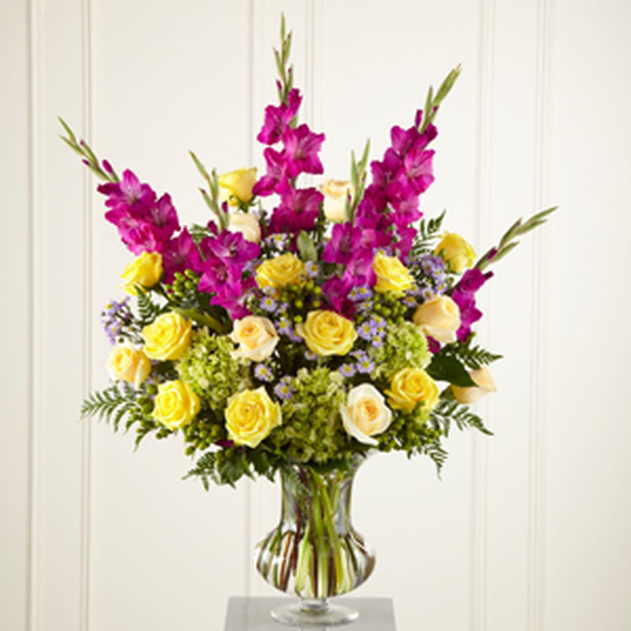 SAFF FTD Loveliness Arrangement SAFF FTD Loveliness Arrangement - Big, colorful, sophisticated. This arrangement makes a fresh and loving tribute to a life lived in beauty and grace. A superb choice for a Memorial or a funeral service. It contains yellow and cream roses, fuchsia gladiolus, lavender monte casino, green hypericum berries and hydrangea with accents of greenery in a premium glass vase.