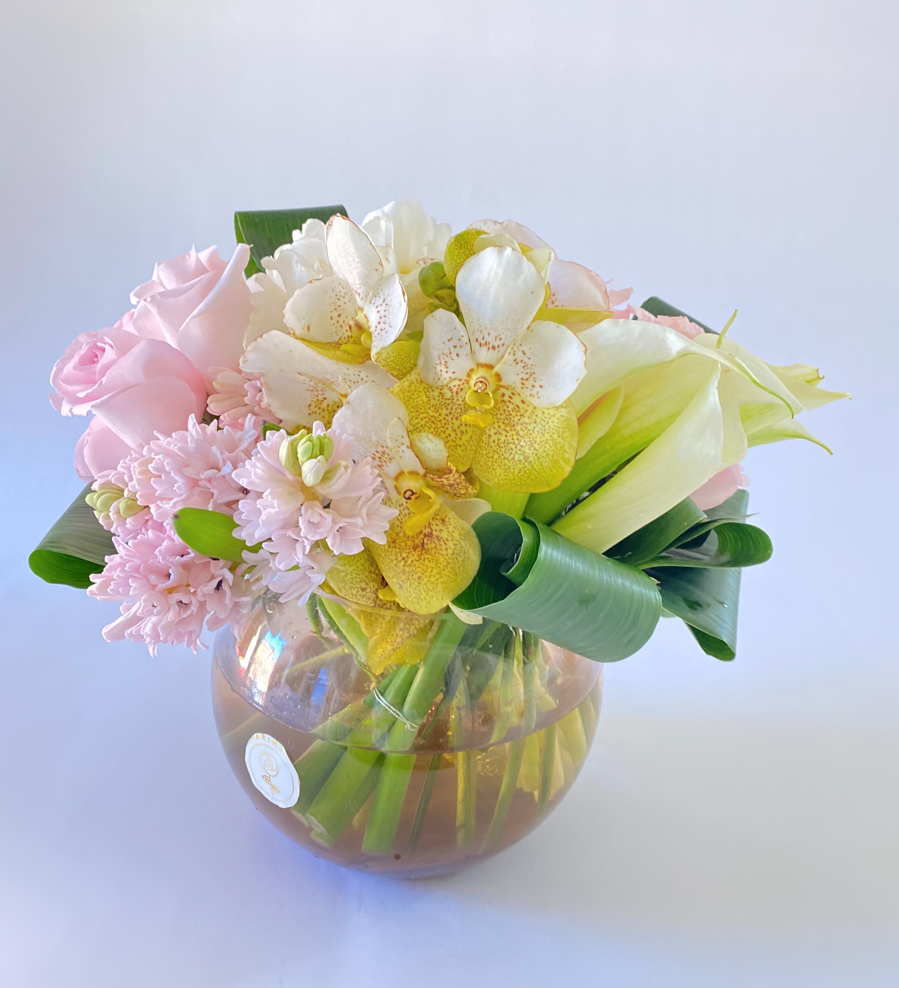 Purely  - This arrangement has beautiful pink roses along with white vandas, calla lilies, and hyacinth these flowers are fragrant and are bundle together nicely in a fishbowl vase filled with sand. This would be the perfect center piece at multiple events. 