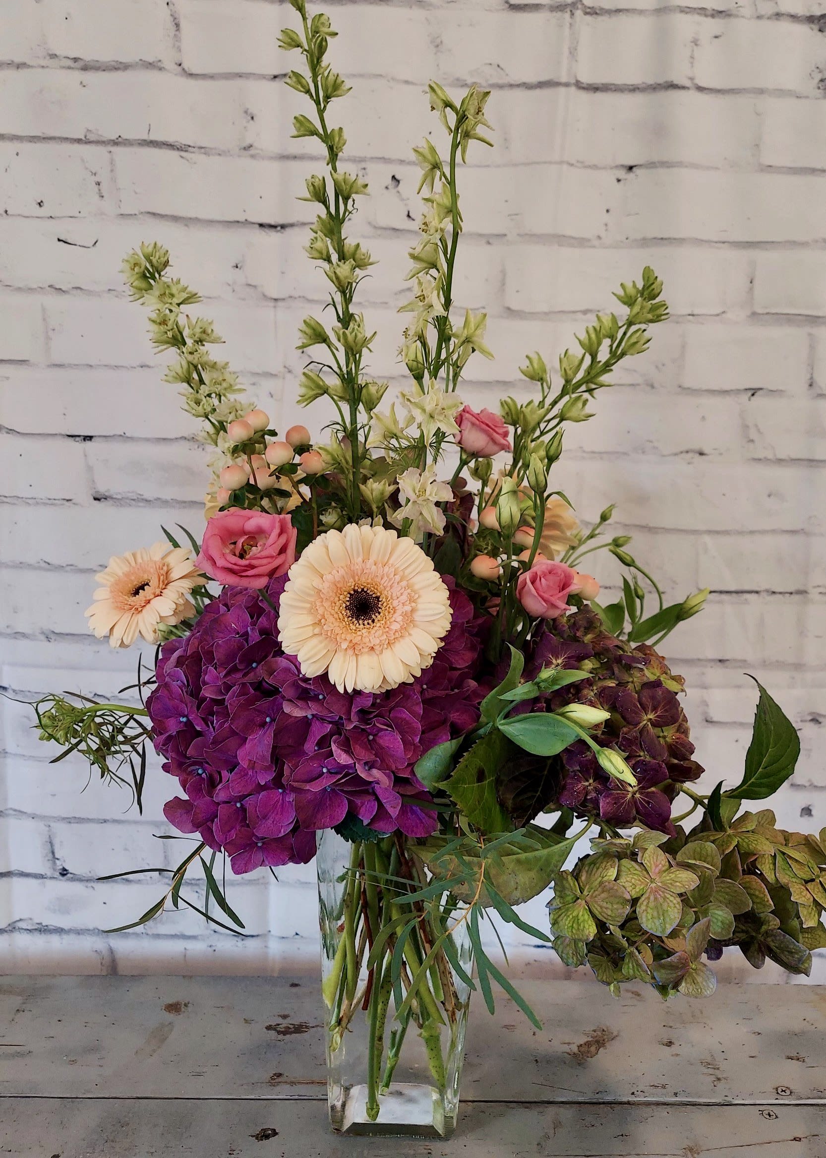 Drama Queen Drama Queen - Dramatic color & presentation makes this custom arrangement a show stopper. Gorgeous plum hues paired with greens and a pop of peach. A special floral arrangement for that special someone!