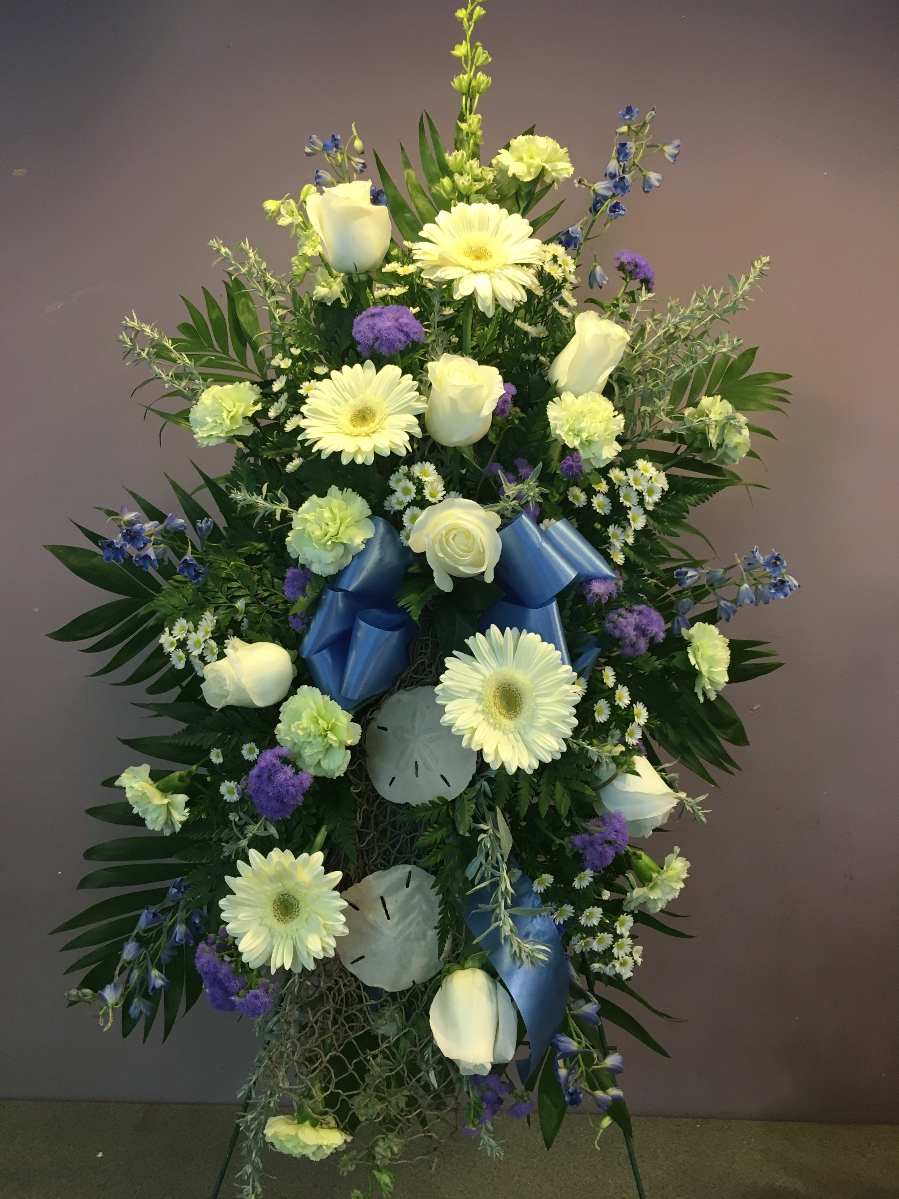 Sea Spray (SS) - A beautiful spray of flowers such as blue delphinium, white roses, green dianthus and other complimenting accent flowers adorned with fishermans net and sand dollars.   Flowers and colors may differ from picture based on availability.