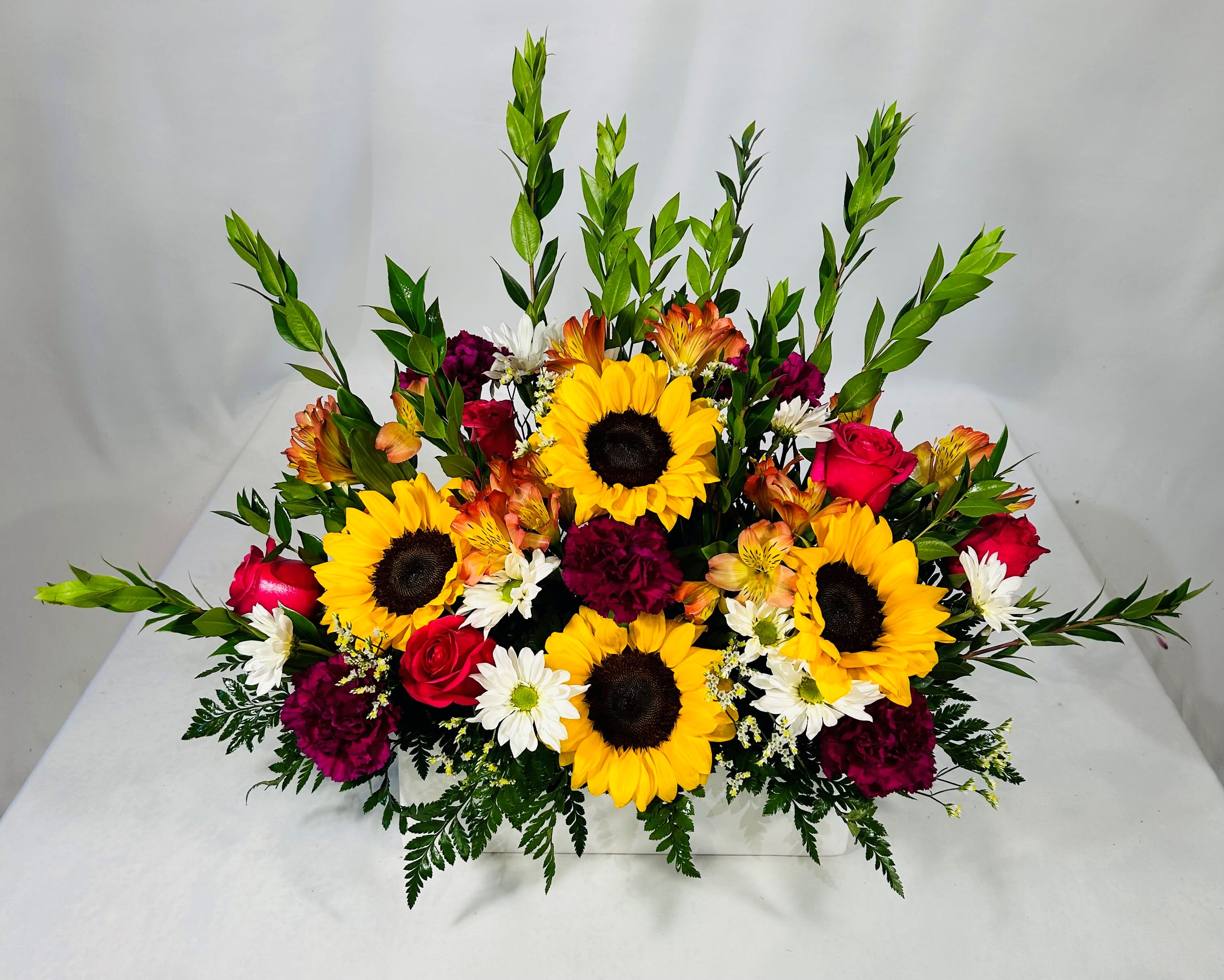 Sunflower Meadow  - Bring the sunflowers from the garden into your home or office with our sunflower, red roses, purple carnations, alstroemeria and white daises  arrangement in a white ceramic container. 