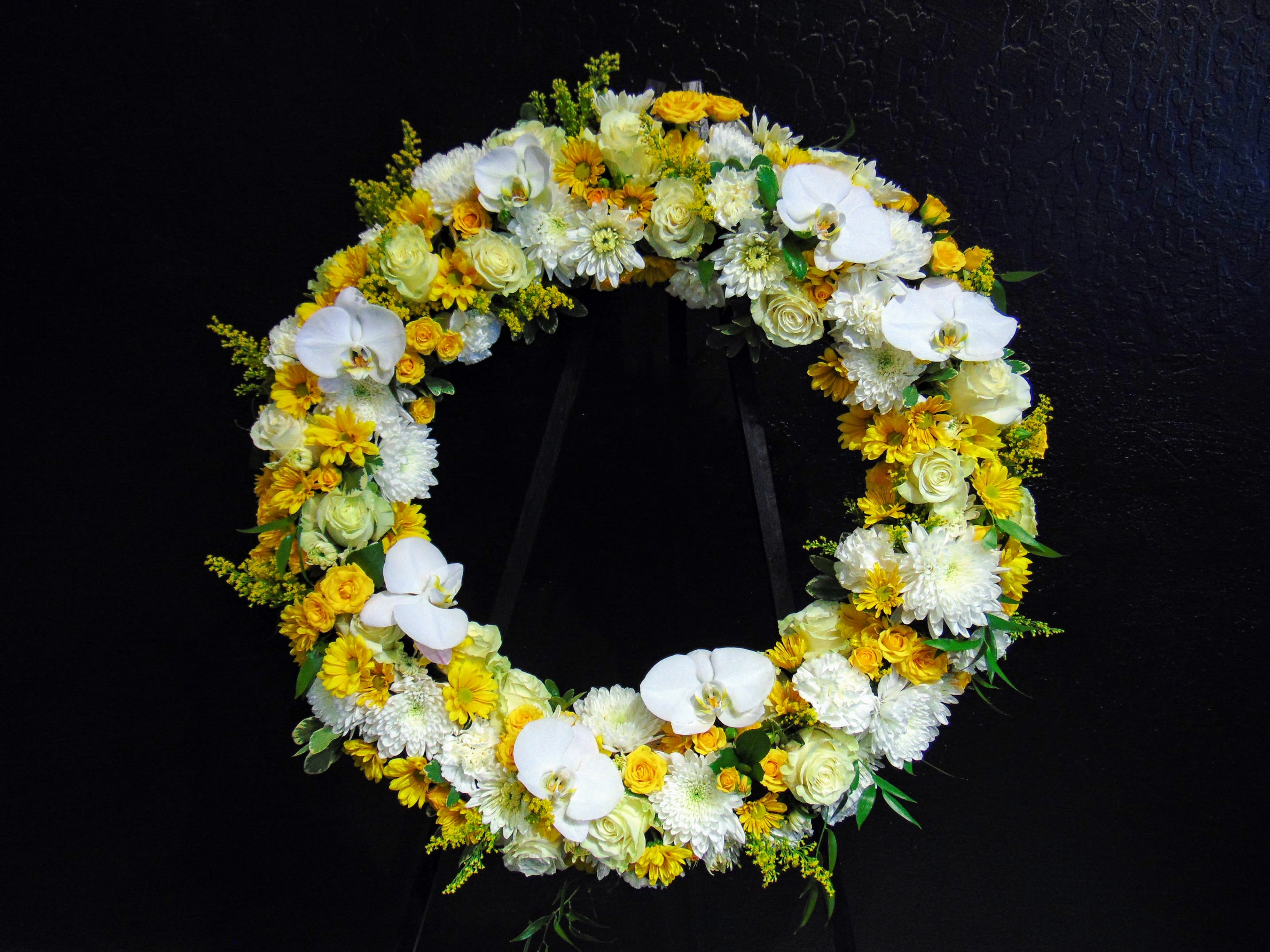 Graceful Wreath - This design is part of our sympathy collection. The softer colors in this design evoke sweet and thoughtful memories. A base of mixed seasonal flowers with accents of orchid blossoms. Pictured is the Deluxe option at 24&quot;.