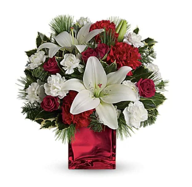 Caroling In The Snow By Teleflora - This festive holiday bouquet includes red roses and white asiatic lilies presented in our red mirrored cube. Red spray roses, white asiatic lilies and red carnations are accented by tips of white pine, noble fir and holly. Delivered in Teleflora's red mirrored cube.   Orientation : All-Around  All prices in USD ($)  Standard  TWR06-1A  Deluxe  TWR06-1B  Premium  TWR06-1C