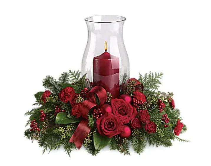 Holiday Glow Centerpiece - Glow ahead and send this spectacular centerpiece to anyone who's on your Christmas list this year. A glowing hurricane candle takes center stage but the surrounding festive touches make this arrangement radiate joy. Beautiful red roses, spray roses and carnations, white asiatic lilies, festive Christmas greenery and ornaments plus an elegant hurricane candle make this divine Christmas décor.   Orientation : All-Around  All prices in USD ($)  Standard  T115-3A  Deluxe  T115-3B  Premium  T115-3C