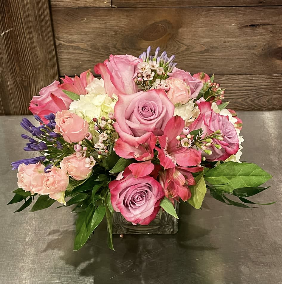 Softly Sweet Softly Sweet - A more compact style arrangement of lavenders, light pinks and whites including hydrangea, roses, spray roses, alstromeria accent flower and greenery in a square vase. Approx. 8" Tall x 8" Wide