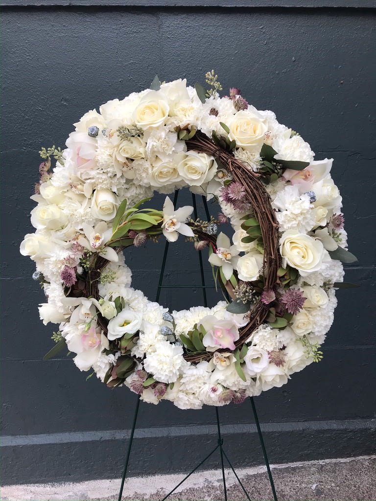 Circle of Life - Winding in a spiral shape of strong dark twigs are a collection of lovely white and light blush pink roses bunched together to give a soft, cloud-like effect. The pastel purples and rich greens that are scattered throughout the arrangement remind us of the adventures of a life well lived. 