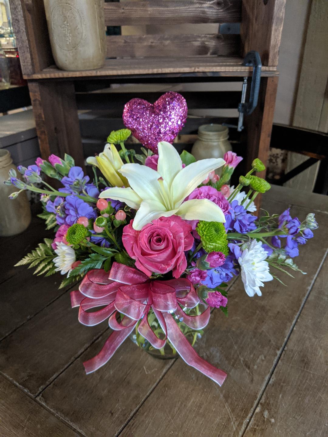 Vivid Love Custom Design by Cold Spring Floral Vivid Love Custom Design by Cold Spring Floral - Vivid Love is a beautiful arrangement of spring colors that is sure to add a touch of Spring to any room! Vivid Love is expertly crafted with a single Pink Rose, Green Kermit mums, Lavenders Stock, White Asiatic Lilies, and Valentines Day accents. All Flowers, Containers, Vases and Accents such as ribbons and picks are subject to substitution based upon availability and will be professionally coordinated to match this style of bouquet.