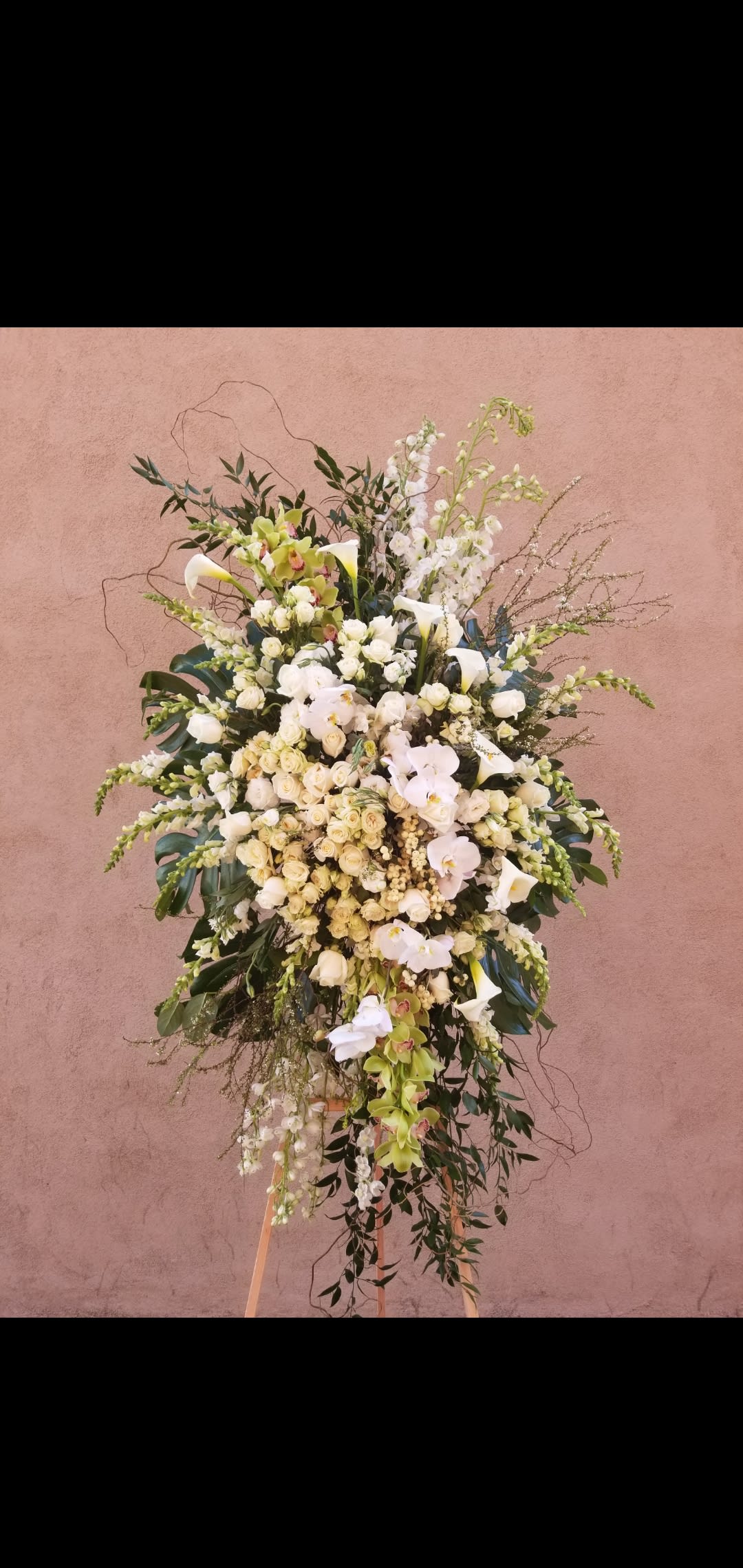 a peaceful goodbye a peaceful goodbye - An all white standing spray, composed of monstera leaves, calla lilly, Phalaenopsis, snap dragons, white roses, spray roses, green cymbidium orchids and delphinum