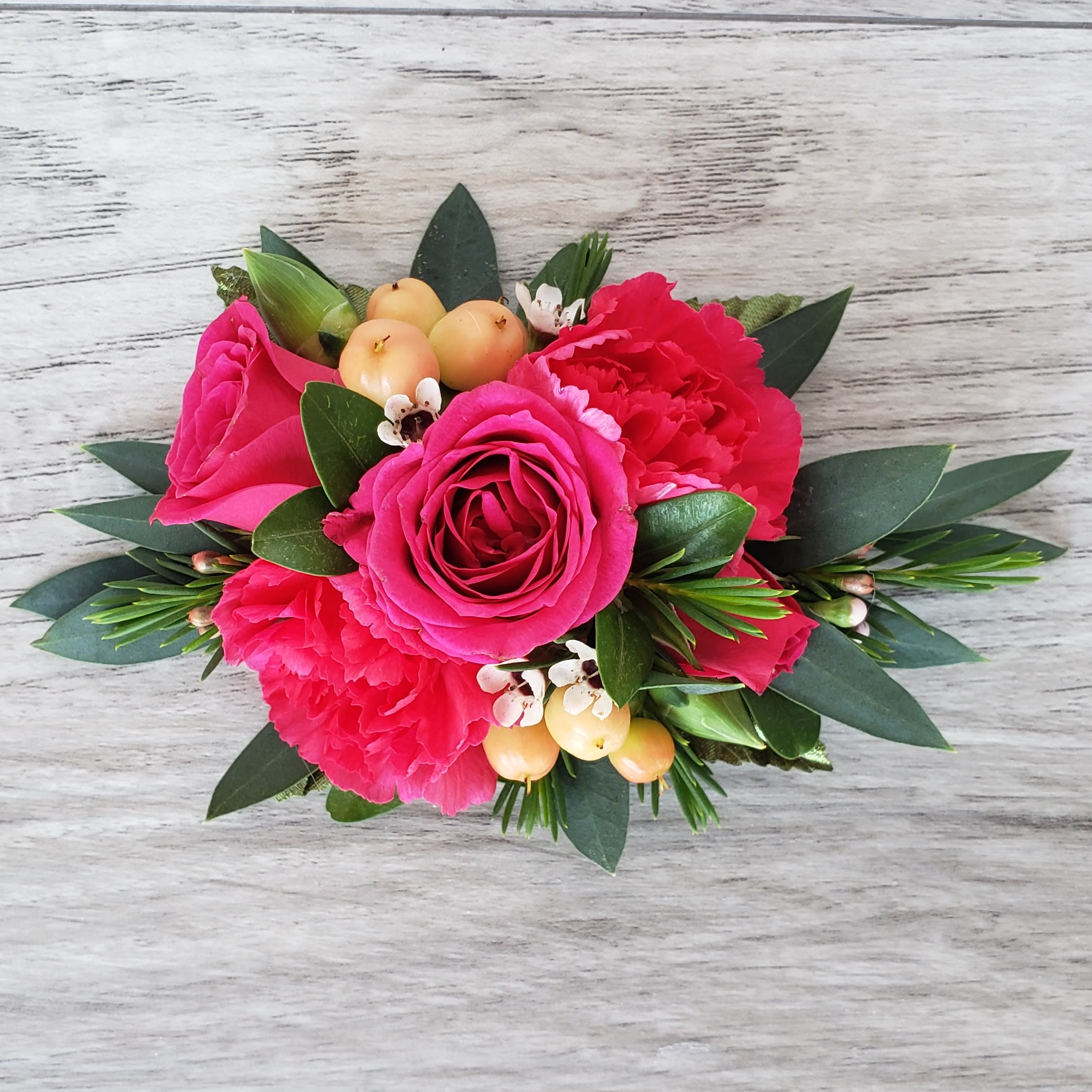 Hot Pink Petite Corsage - This corsage is more petite in size and features hot pink spray roses, peach hypericum, hot pink mini carnations and complementary greens and accent flower.If you would like to exchange the colors of the flowers please let us know and we will be happy to accommodate.