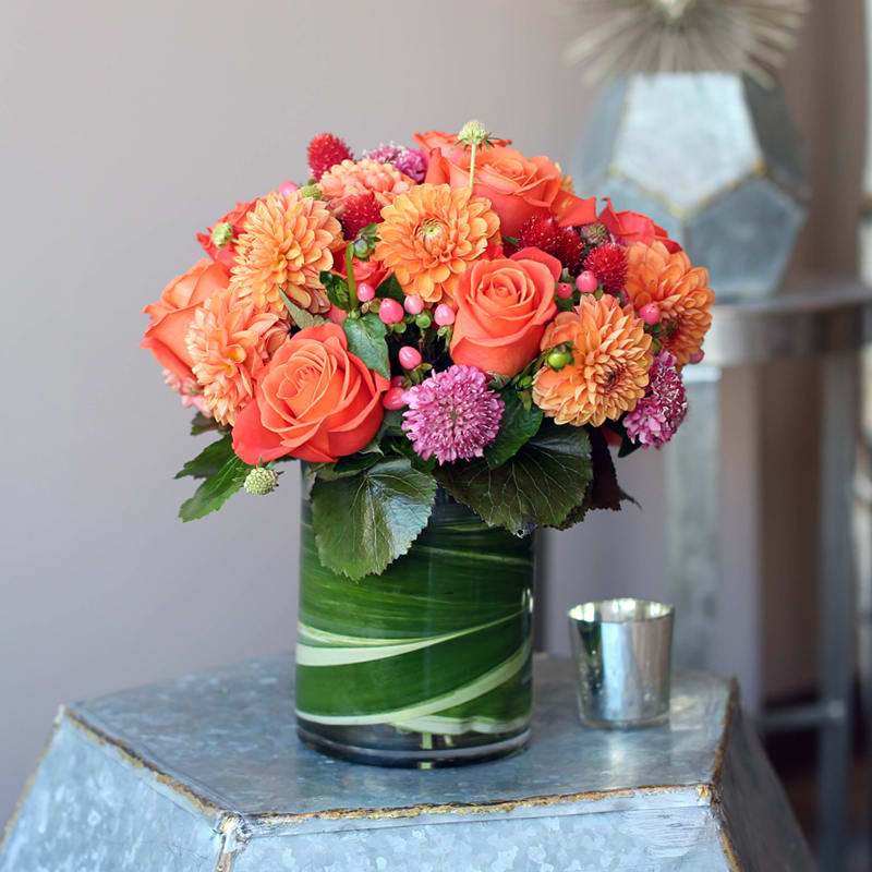 FABULOUS FALL - SHADES OF ORANGE FLOWERS SUCH AS ROSES, DAHLIA, HYPERICUM BERRIES AND MORE IN A CYLINDER VASE WITH LEAF IN WATER