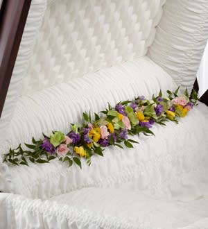 Trail of Flowers Casket Adornment  - Is a gorgeous accent piece that offers an extra touch of floral beauty at their memorial service. Green hydrangea, pink spray roses, yellow freesia, lavender larkspur and yellow button poms are arranged to bedeck the inner lining of the casket creating a soft and elegant look that perfectly commemorates the life of the deceased.