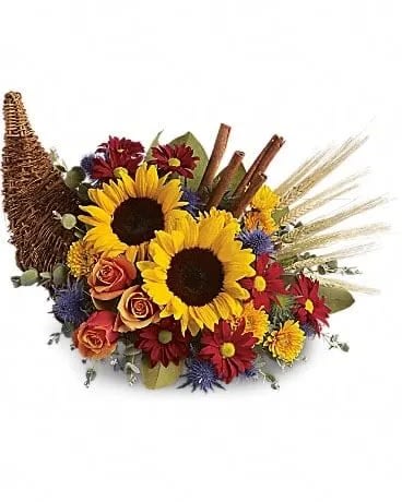 Classic Cornucopia - Along with joy, this cornucopia carries an abundance of beautiful fall flowers and foliage. A stunning centerpiece or inviting entryway display, this beauty will be at home anywhere in the house. Dazzling sunflowers, light orange roses and spray roses, red daisy spray chrysanthemums, yellow cushion spray chrysanthemums, eucalyptus, magnolia leaves, cinnamon sticks and wheat are perfectly arranged in a wicker cornucopia. Now you know why cornucopia translates to &quot;horn of plenty.&quot; 
