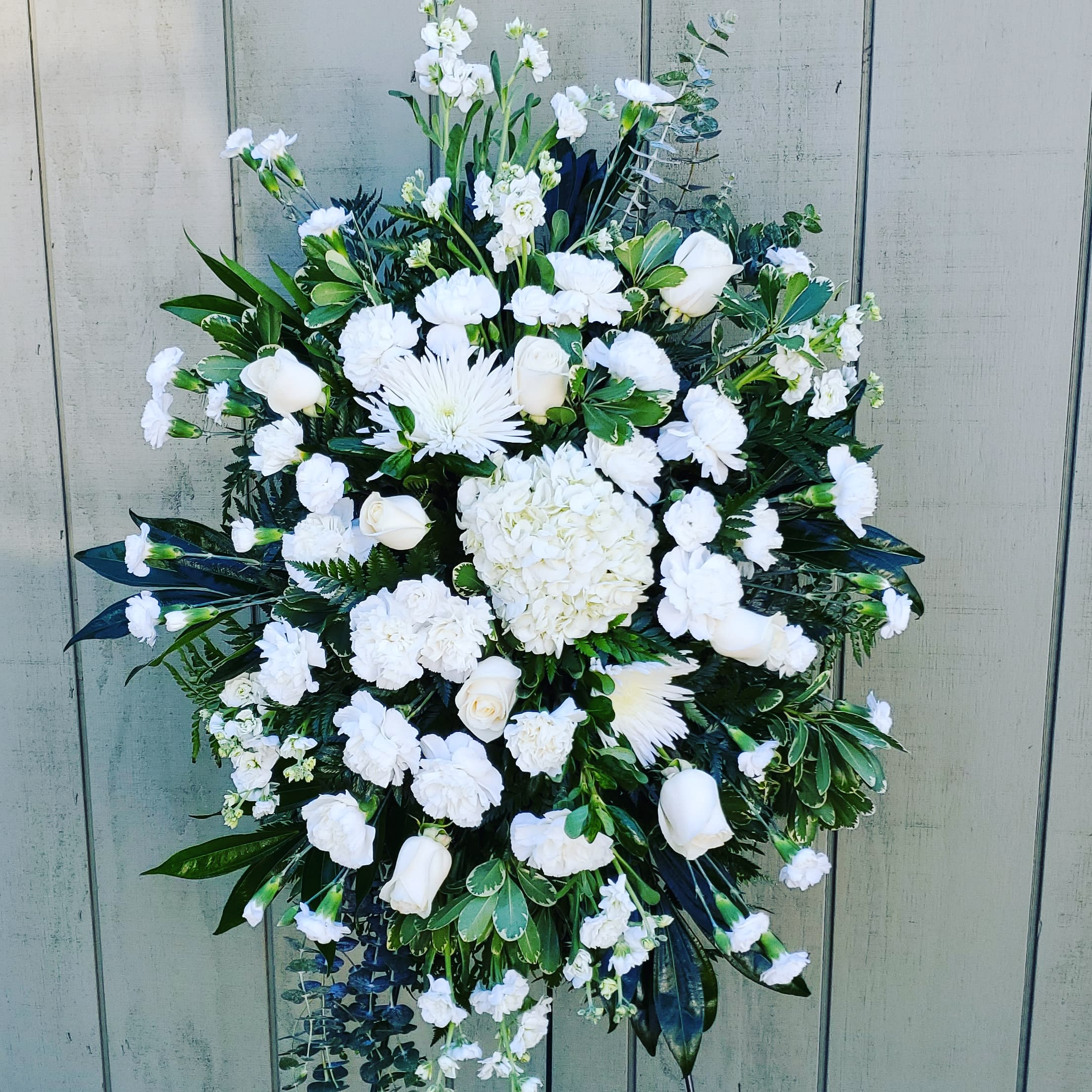 Forever in Our Hearts Funeral Spray Forever in Our Hearts Funeral Spray - Standing Spray is an elegant display of sweet serenity. White roses, chrysanthemums, carnations, and mini carnations are artfully arranged amongst emerald palm fronds centerned with a hydrangea lush greens. Accented by white satin ribbon and standing on a wire easel, this standing spray is an outstanding way to honor the life of your loved one. GOOD spray is approximately 32"H x 20"W. *Available in any color or color combination
